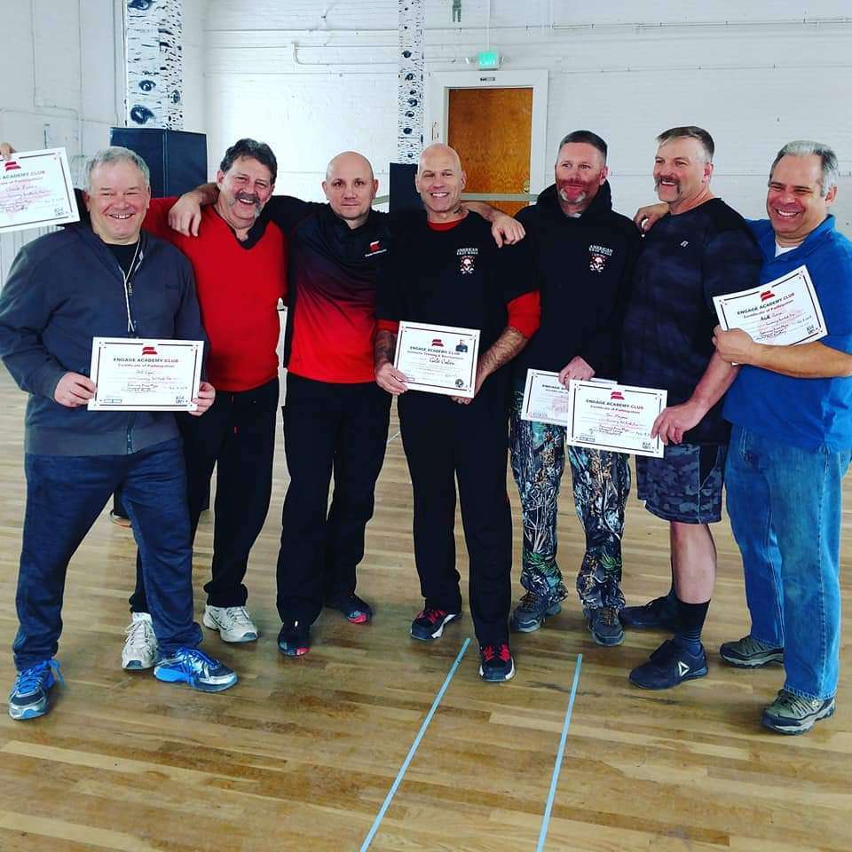 A group of men holding Krav Maga certificates in a gym during an interview.